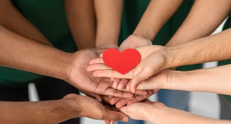 Hands joined together holding a red paper heart